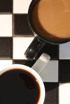 Top view of black and white coffee mugs full of coffee on a black and white checkered background.