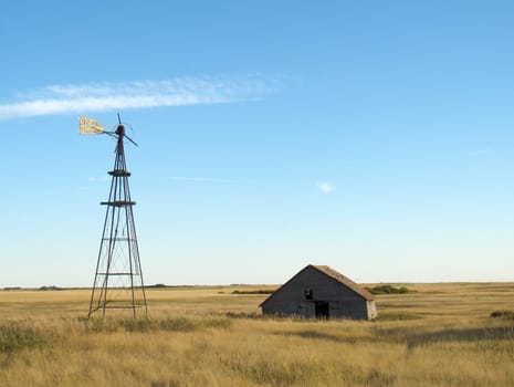 Abandoned building and broken down windmill in a field.