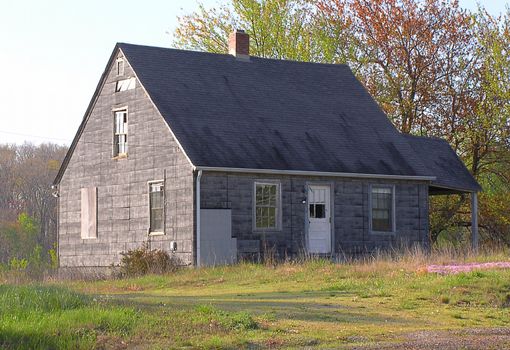 A house in a rural area, found in a state of disrepair. The side porch slumps slightly, some windows are broken and siding missing, but outward appearance is that this could be reinhabited with some repair work.