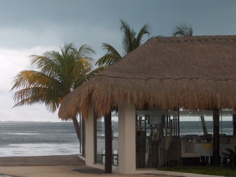 A thatched restaraunt at a resort in Mexico, overlooking the ocean on a stormy day.