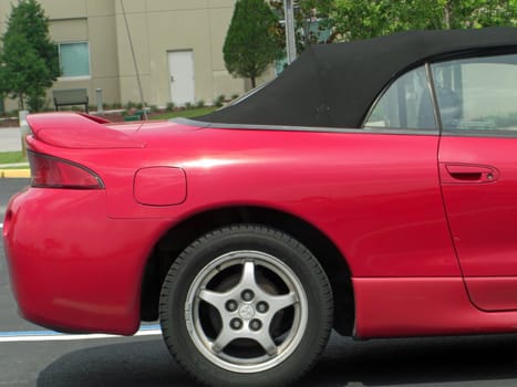 A red, two door, Ford Mustang, convertible and fuel efficient  car is parked in a parking lot.