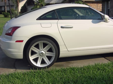 A white, two door, compact, fuel saving Dodge is parked in a driveway.