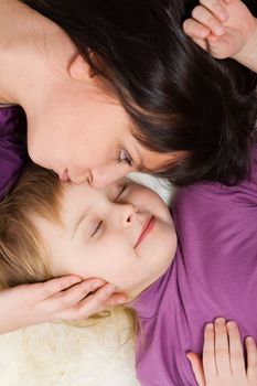 Mother kissing sleeping daughter lying heads only