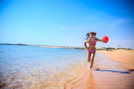 Girl Running on sunny beach with red balloon