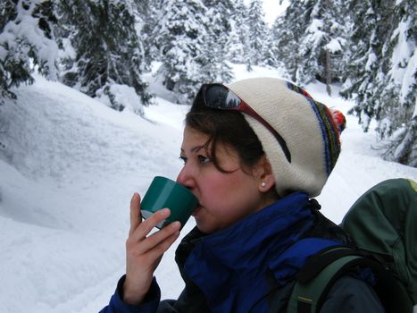 a young woman drinking a warm drink in the snow