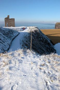 a seasonal snow covered view of atlantic ocean and ballybunion castle beach and cliffs on a frosty snow covered winters day
