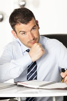 pensive young businessman with pen in office
