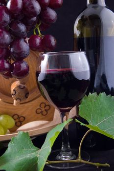 Red wine bottle, glass and cask with grapes over black
