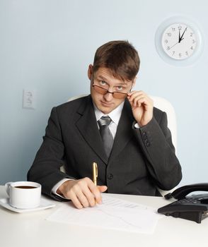 Serious young businessman in office looking above glasses