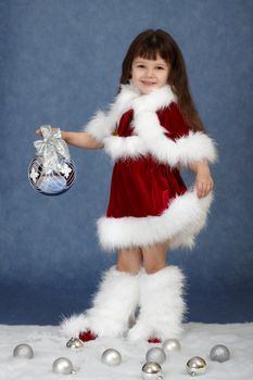 The little girl in a Christmas costume with glass ball on a blue background