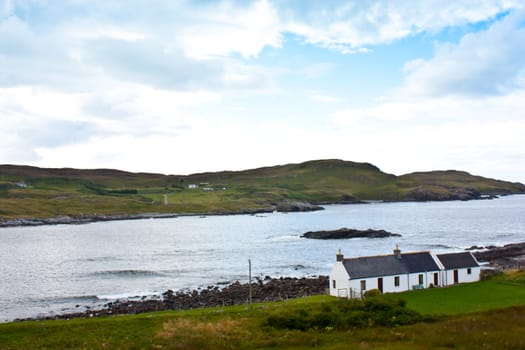 Panorama with a traditional Scottish house in front of a lake.