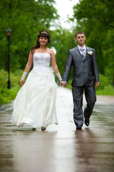 Bride and groom walking in summer park outdoors