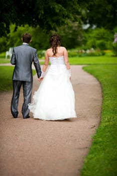 Bride and groom walking away in summer park outdoors