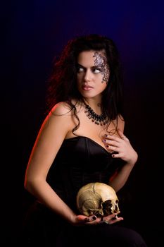 Young beautiful demonic female creature holding scull