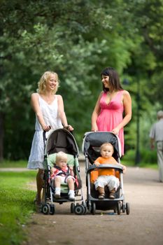 Happy mothers walking together with kids in prams 