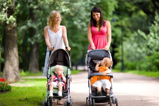 Happy mothers walking together with kids in prams 