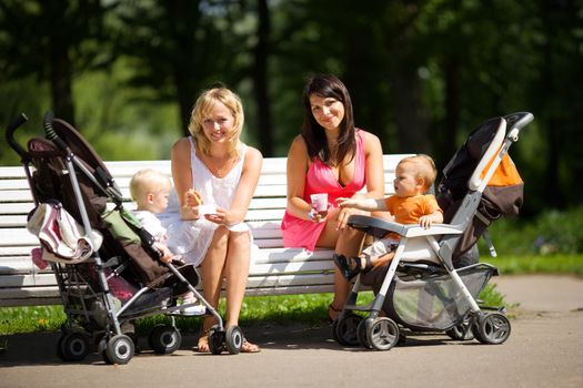 Two mothers spoon feeding their babies sitting on bench