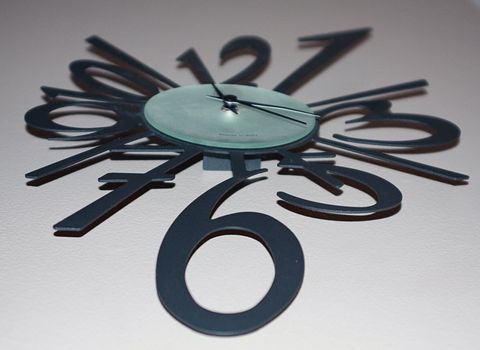 Modern abstract wall clock with large numbers and hands. Wall clock isolated on off-white background. Home decoration for keeping time.