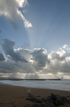 Big sunlight rays through big clouds above a jetty during a stormy day