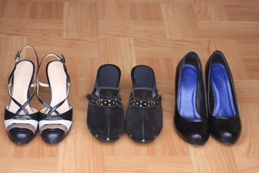 Three pairs of black women’s shoes lined up on wood floor by door. Attractive women’s foot wear for fashion, home and shopping.