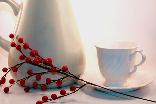 White tea pitcher and teacup with holly berries isolated on white background. Tea and coffee for holidays or special occasion.