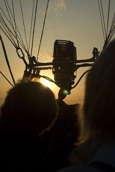 black silhouettes of people in an hot air balloon, burner with fire 