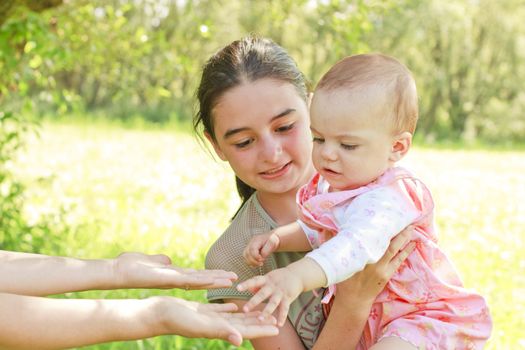 A teenager with a baby in her arms give the child to her mother