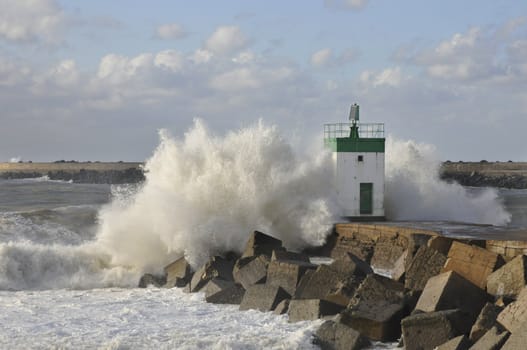 Big wave on a blocks jetty with a little lighthouse