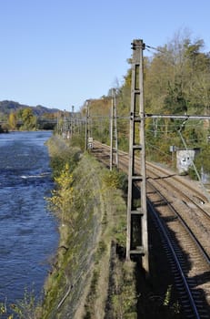 Rails and pickets along a river with trees and a blue sky