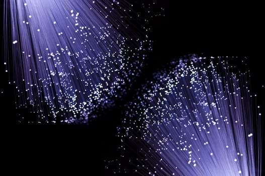 Close up capturing the ends of many illuminated fibre optic light strands against a black background.