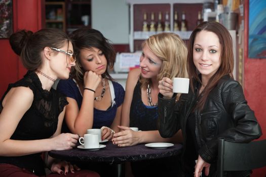 A confident young woman drinks coffee with friends in a cafe