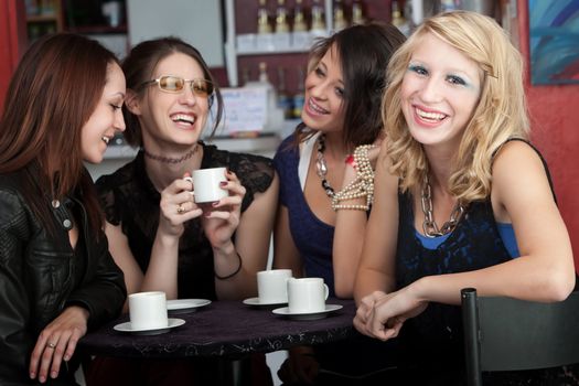 A cute blonde girl smiles while sitting with three friends in a cafe