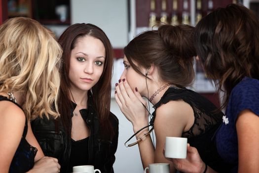 In a group of four cute girls, a friend whispers something to another in a cafe