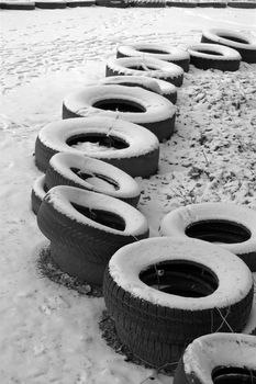 The row of the old tires. Serve on the side limiter training track. Winter season. Black and white 