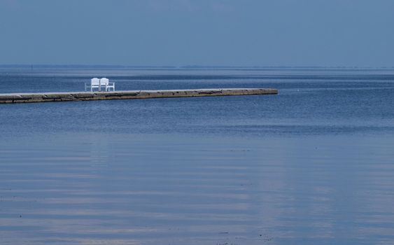 white bench on a pier amidst blue calm water
