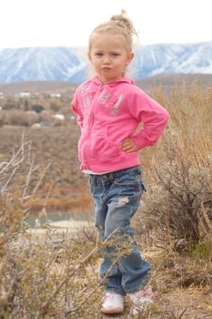 A serious young girl, posing in front of the mountains.  She has her hands on her hips.