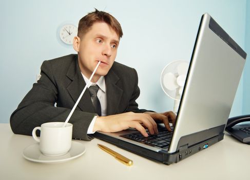 The amusing businessman drinks coffee through a straw without distracting from work in the Internet