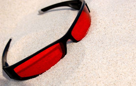 Red sunglasses lying on a sandy beach. Vacation photo.