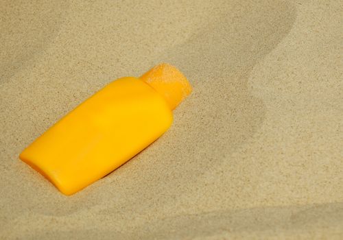 Yellow blank sunscreen bottle lying on sandy beach