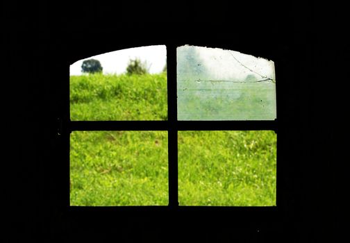 Broken window. View on green fields from dark room