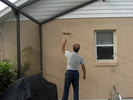 A man is painting a screen enclosed area of his house, using a paint roller