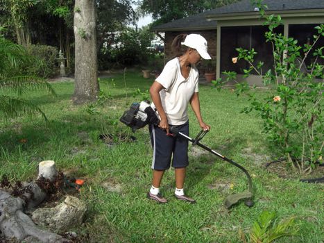 To make ends meet, a woman with a lawn mowing services is trimming the grass with a weed wacker.