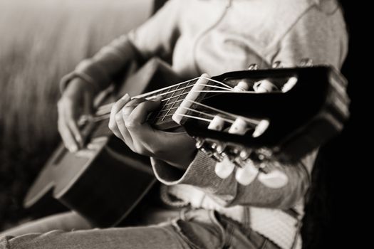 Woman playing her guitar at the sunset (focus is on the left hand) Toned in PS