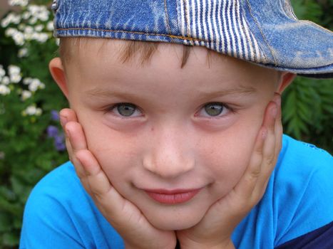 Little boy clenched by palms his face. It seems that he awaits something, fixedly looking into your eyes.