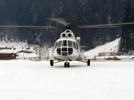 helicopter landed among the Carpathian mountains, raising snowflakes into air. 