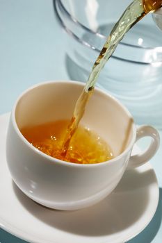 flowing golden tea into cup over blue
