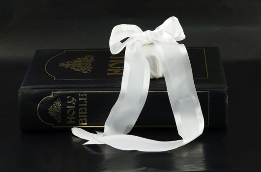 Large family Bible with white gift wrapped in white satin ribbon on simple, black background represents a cherished family event