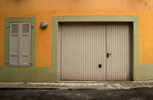 Closed garage door and window with closed shutters in a pink facade in a street