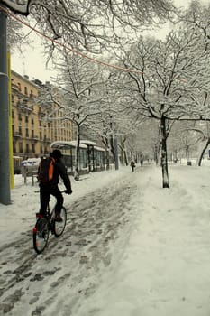 Biker driving its bike on the snow in a city park near buildings by wintertime