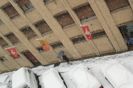 Walker hanging an umbrella walking in a street next to cars covered with snow by winter time in Geneva, Switzerland